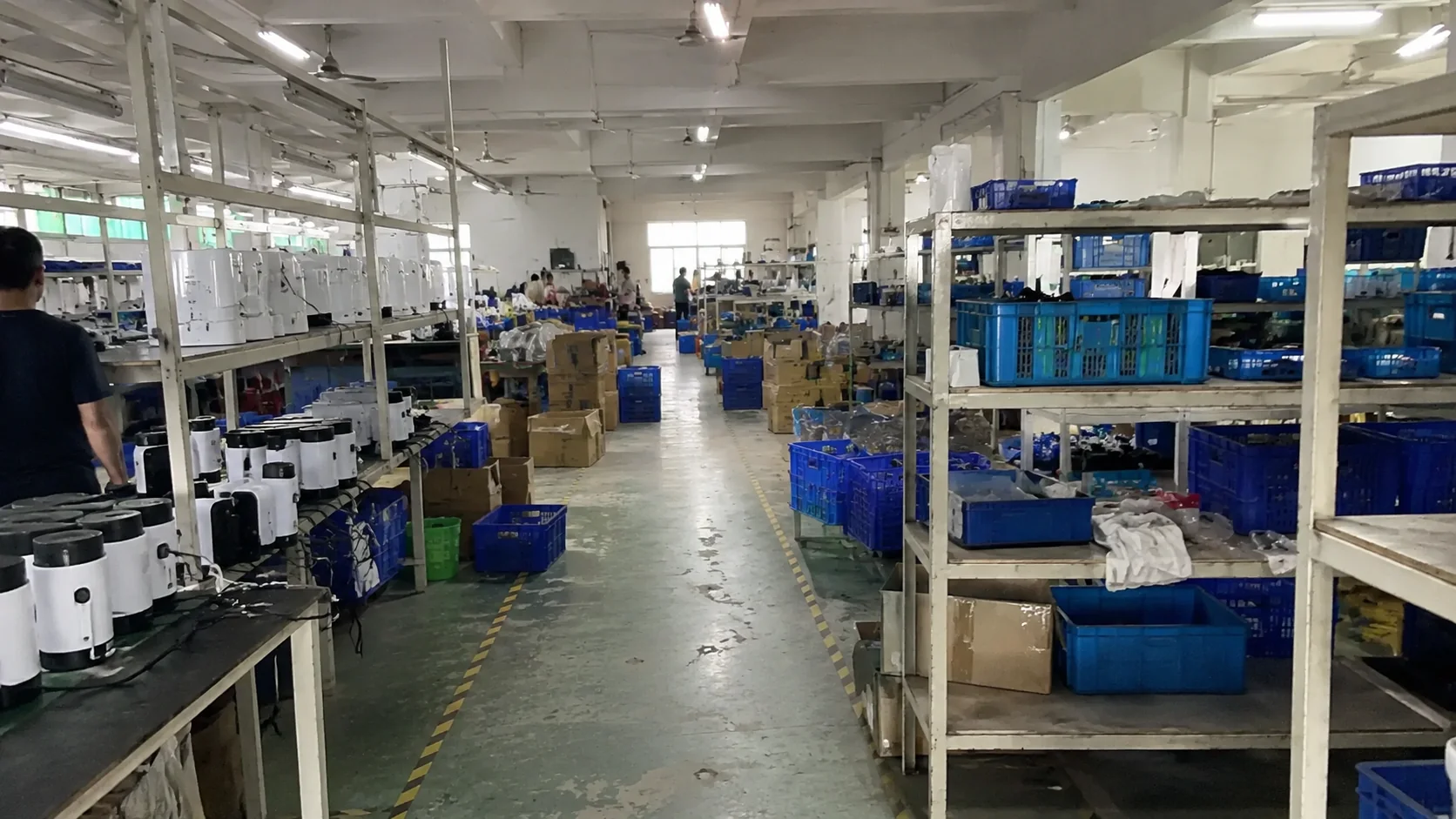 Factory aisle with assembly benches, shelves, product parts, and carton staging